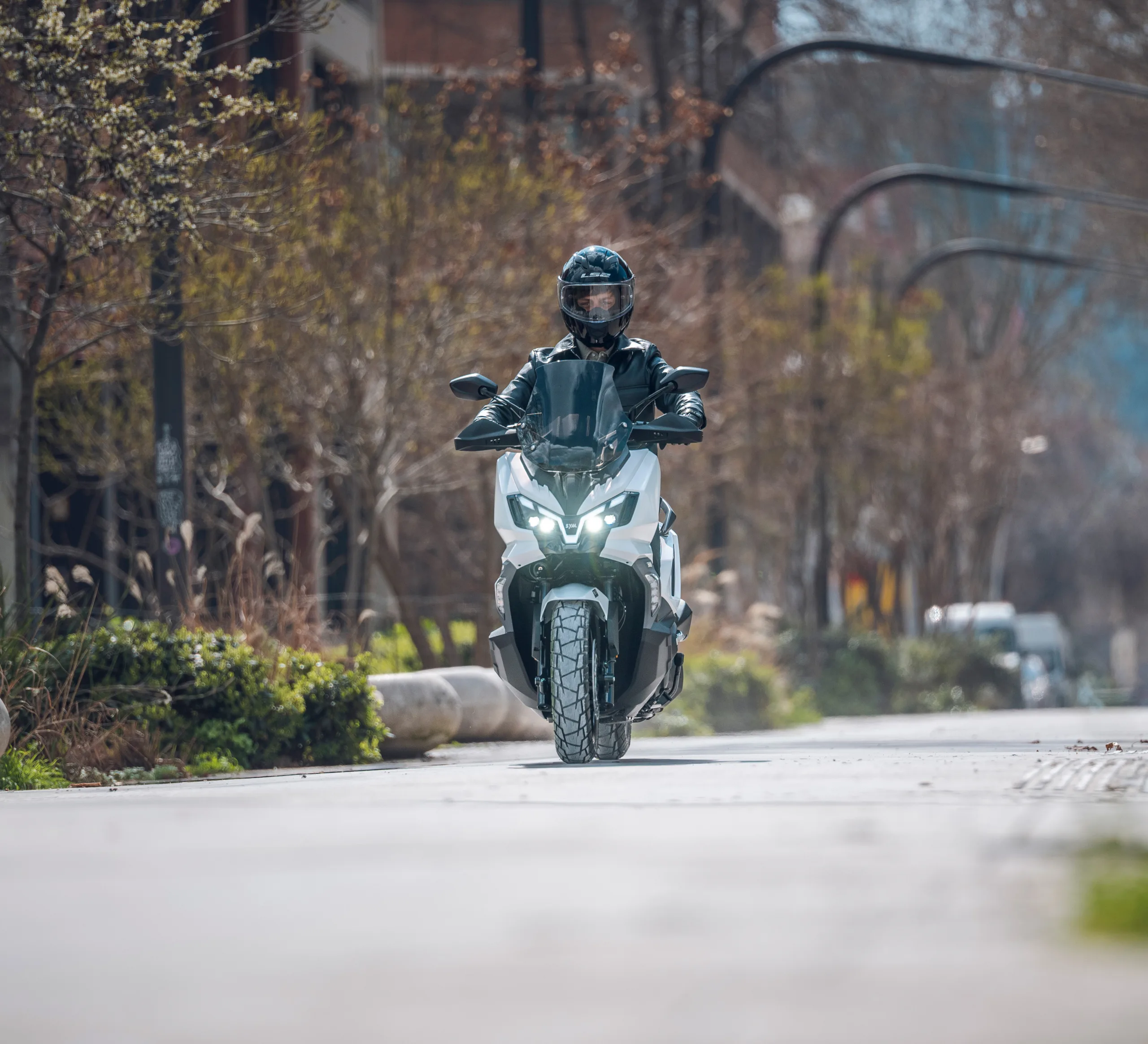 Motociclista conduciendo una motocicleta SYM en una calle urbana con árboles y edificios de fondo
